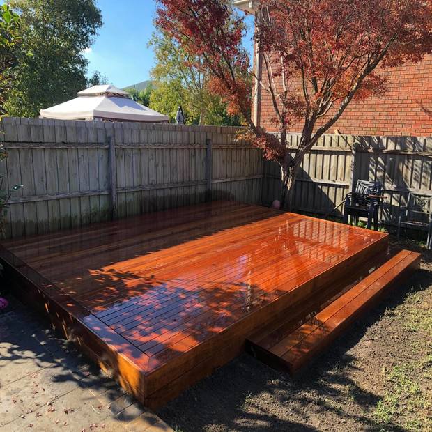 A Merbau timber decking in a backyard next to a tree and some chairs.