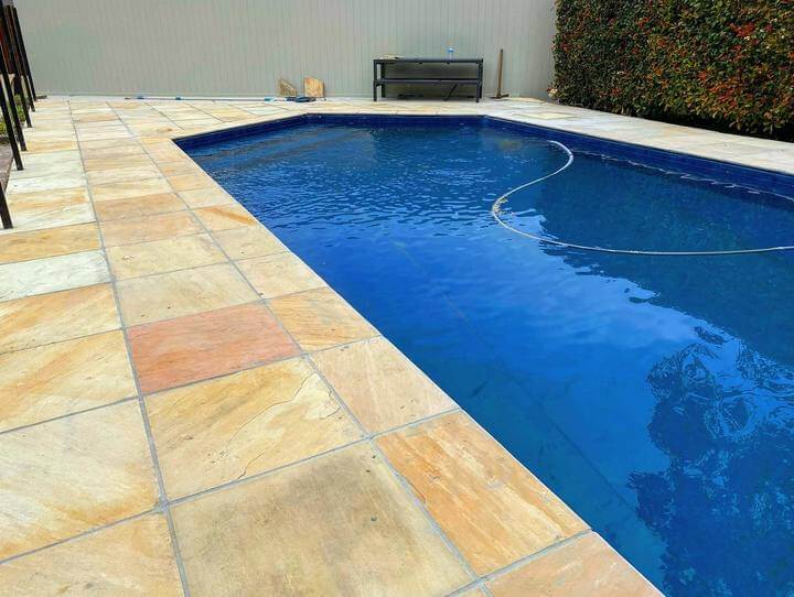 Sandstone pavers next to a blue pool with a water hose in the pool.